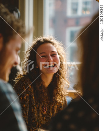A woman with curly hair smiling, sitting in a bright room with two other people. 130109345