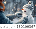 A person is putting the finishing touches on a small snowman wearing a hat in snowy weather. 130109367