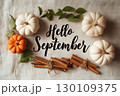 Small pumpkins and bundles of cinnamon sticks on a textured fabric with 'Hello September' written in elegant script. 130109375