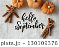 Small pumpkins and bundles of cinnamon sticks on a textured fabric with 'Hello September' written in elegant script. 130109376