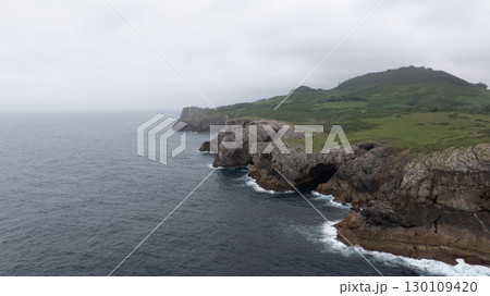 Dramatic cliffs and lush green hills meet the vast expanse of the Cantabrian sea along the rugged coastline of Asturias, Spain, creating a breathtaking vista 130109420