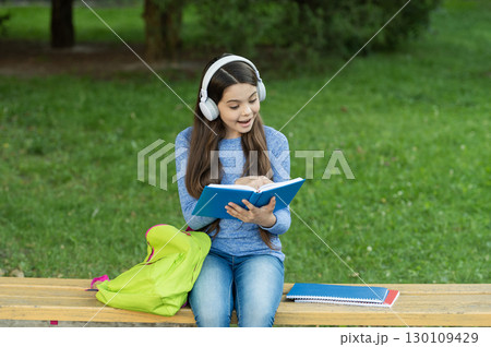 Girl listen audiobook and read book. Audiobook vs book. Student girl. School education. School girl read book and listen audiobook outdoor. Back to school. Education and knowledge. Be curious 130109429