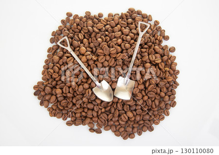 Close-up of intersecting stainless steel shovels on a textured layer of dark roasted coffee beans 130110080