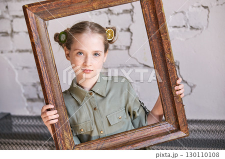 Young caucasian female child holding rustic frame with brick wall background 130110108