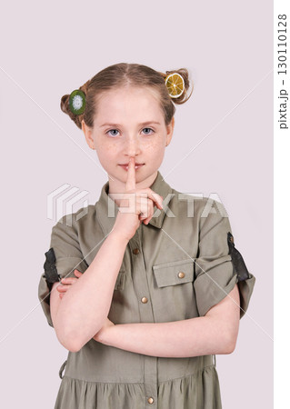 Caucasian young girl in green dress with finger on lips making silence gesture 130110128