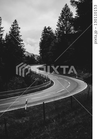 A curving road cuts through a lush forest, shrouded in clouds. The landscape features tall trees lining the highway, creating a serene atmosphere during the overcast weather. 130110153