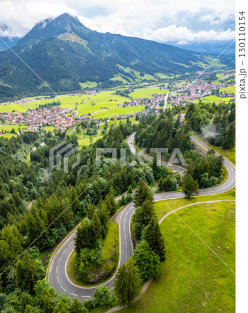 Experience the breathtaking curves of alpine serpentines as they meander through lush greenery and lead towards distant mountains. A memorable journey on a scenic road awaits. 130110154