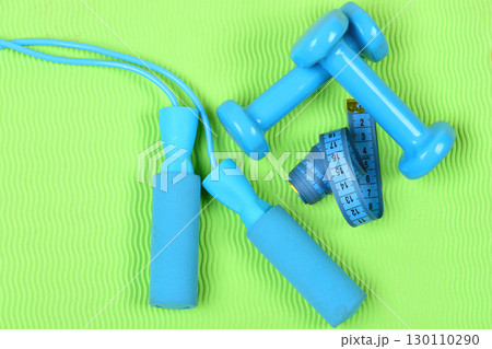 Dumbbells and jump rope in cyan color on green background Dumbbells and jump rope in cyan color on green background 130110290