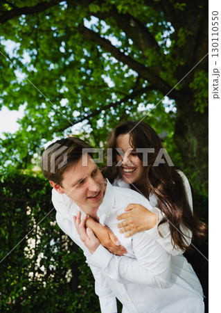 Young couple enjoying playful moment outdoors, surrounded by lush greenery and bright sunlight Young couple enjoying playful moment outdoors, surrounded by lush greenery and bright sunlight 130110550
