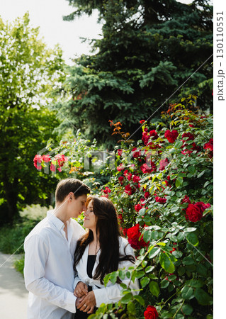 Young loving married couple embracing in a garden surrounded by vibrant red roses and greenery Young loving married couple embracing in a garden surrounded by vibrant red roses and greenery 130110551