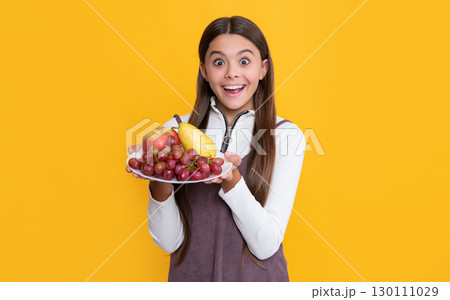 surprised child hold fruit plate on yellow background 130111029