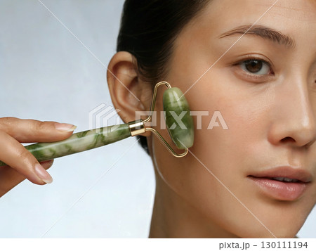 Woman using jade stone jade roller for facial massage beauty wellness skincare and rejuvenating natural selfcare treatment 130111194
