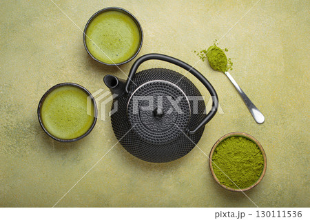 Matcha tea powder and hot drink in bowls with black iron teapot on green background, Japanese tea top view Matcha tea powder and hot drink in bowls with black iron teapot on green background, Japanese tea top view 130111536