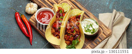 Mexican tacos with chili con carne, red beans, and lime wedges on wooden board top view 130111551