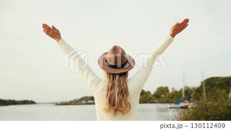 Happy stylish woman traveler on beach, enjoying warm weather, wear hat standing on sea coast 130112409