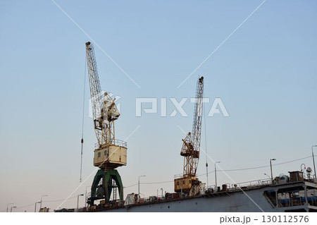 Industrial Cranes Skillfully Operating at Dusk Within a Busy and Vibrant Shipyard Environment 130112576