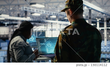 Soldier in engineering role uses AI application on laptop to manage server hub systems. Army commander reviews secret intelligence information using artificial intelligence in data center, camera B 130114112