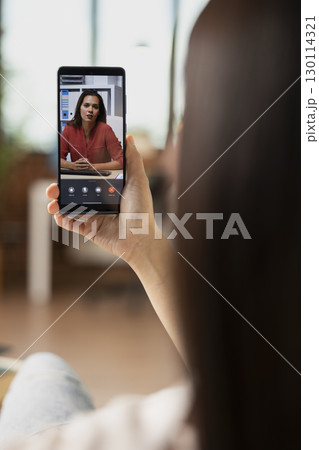 Self employed woman discussing with remote coworker on mobile device. Professional freelancer with smartphone in hand, brainstorming business project during virtual conversation with female investor. 130114321