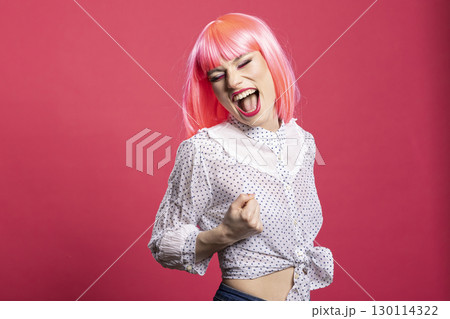 Joyful caucasian lady expressing excitement with mouth open and fist raised, standing isolated over pink background. Beautiful happy woman filled with enthusiasm, celebrating good news and success. Joyful caucasian lady expressing excitement with mouth open and fist raised, standing isolated over pink background. Beautiful happy woman filled with enthusiasm, celebrating good news and success. 130114322