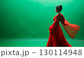 A figure in elegant traditional garments exuding grace in front of a rich green backdrop 130114948