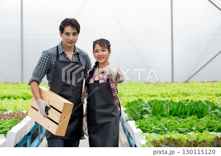 Confident Asian farmers standing in a smart greenhouse with fresh organic vegetables, smiling and showing thumbs up, representing success in modern farming and sustainable agriculture. 130115120