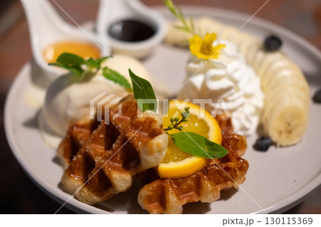 Waffle with vanilla ice cream served with sliced banana , whipped cream and sauce. Waffle with vanilla ice cream served with sliced banana , whipped cream and sauce. 130115369