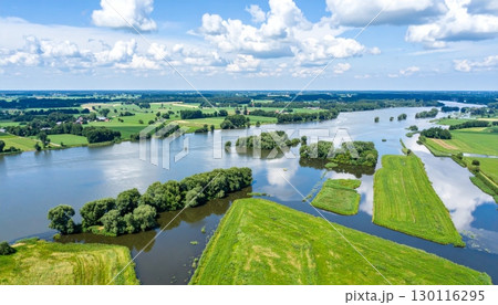Beautiful summer landscape with a calm river reflecting the blue sky, green trees, and clouds Beautiful summer landscape with a calm river reflecting the blue sky, green trees, and clouds 130116295