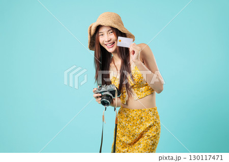 Happy Asian woman ready to travel, holds her bank credit card, camera and blank payment card to make online payment, cheerful tourism holiday smile girl, headshots isolated studio blue background 130117471