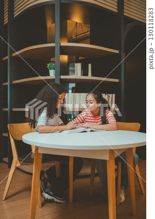Teenage girls studying together in modern library showing concentration teamwork and educational motivation Teenage girls studying together in modern library showing concentration teamwork and educational motivation 130118283