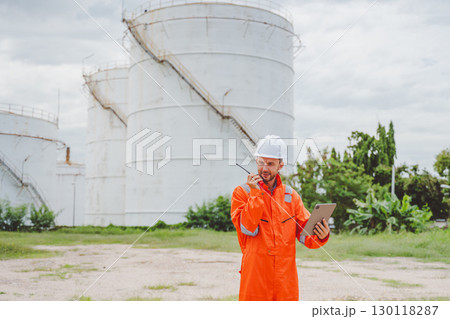 Field engineer using tablet and radio to coordinate inspection at oil storage tanks Field engineer using tablet and radio to coordinate inspection at oil storage tanks 130118287
