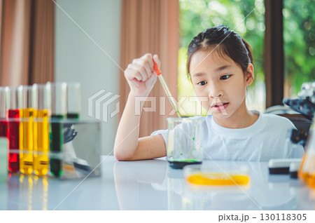 little scientist looking through a microscope and test tubes filled with chemicals for learning about science and experiments. 130118305