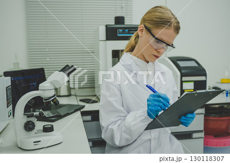 Female scientist taking notes on clipboard in laboratory while conducting biology medical research for science and education Female scientist taking notes on clipboard in laboratory while conducting biology medical research for science and education 130118307