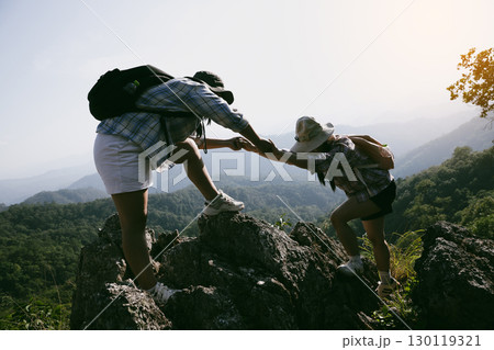 Two friends helping with teamwork trying to reach top of mountains during wonderful summer sunset. Teamwork couple hiking help each other trust assistance. Team of climbers two friends hiker. 130119321