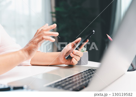 Close-up shot, woman sits at a wooden table using her smartphone, with her finger touching the phone screen as she navigates mobile banking, online shopping, and social media networks. Close-up shot, woman sits at a wooden table using her smartphone, with her finger touching the phone screen as she navigates mobile banking, online shopping, and social media networks. 130119582
