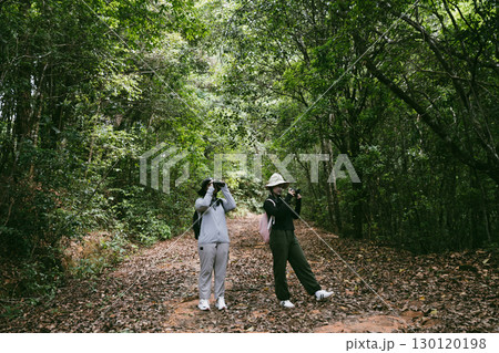Two female friends with backpacks on vacation hiking through countryside together. Asian friend girls backpacker friend travel in forest wild together. happy and enjoying sunny day while hiking. 130120198