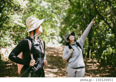 Two female friends with backpacks on vacation hiking through countryside together. Asian friend girls backpacker friend travel in forest wild together. happy and enjoying sunny day while hiking. Two female friends with backpacks on vacation hiking through countryside together. Asian friend girls backpacker friend travel in forest wild together. happy and enjoying sunny day while hiking. 130120851