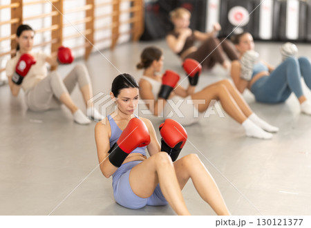 Young girl doing abdominal exercise with boxing gloves in group Young girl doing abdominal exercise with boxing gloves in group 130121377