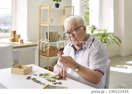 Senior man with dementia sitting at table, playing games and trying to solve puzzles Senior man with dementia sitting at table, playing games and trying to solve puzzles 130121435