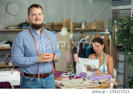 Bearded tailor with measuring tape posing in sewing studio 130121521