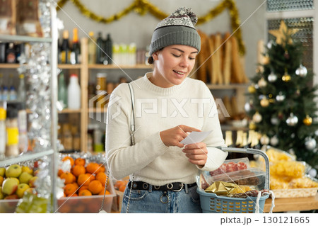 Feale customer prepares to celebrate Christmas - they buy food and alcohol according to checklist at supermarket 130121665