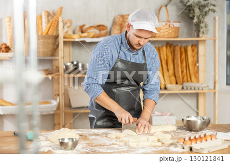 Professional baker uses knife to cut raw dough to make croissants or buns 130121841