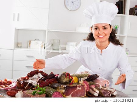 Girl cook costs near table on which sausages and smoked meat 130121921