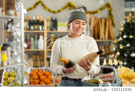 Happy young woman choosing wine in Christmas decorated store 130121936