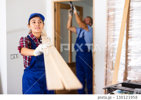 Positive woman builder carrying wooden planks in construction site 130121958