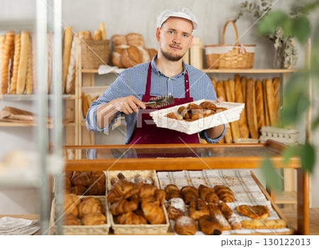 Selling fresh croissants in bakery - Baker places hot croissants on display Selling fresh croissants in bakery - Baker places hot croissants on display 130122013