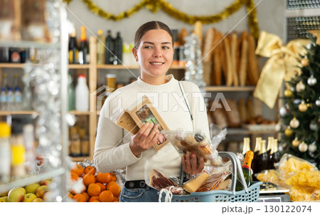 Smiling young woman choosing sweets for Christmas feast in decorated store 130122074