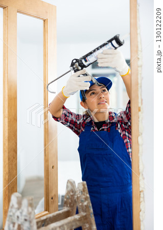 Experienced female door installer fills gaps with mounting foam 130122209