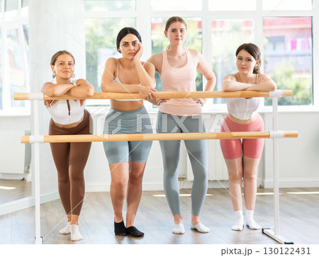 Young female ballet students relaxing at barre in studio 130122431
