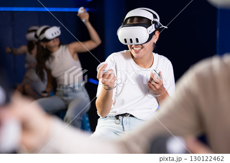 Girls is enjoying exciting game with friends in VR glasses in entertainment dark room 130122462