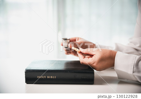During the holy communion ceremony in church, a hand is extended in faith to receive the sacred sacrament, reflecting the spiritual and religious worship central to Christianity. 130122928